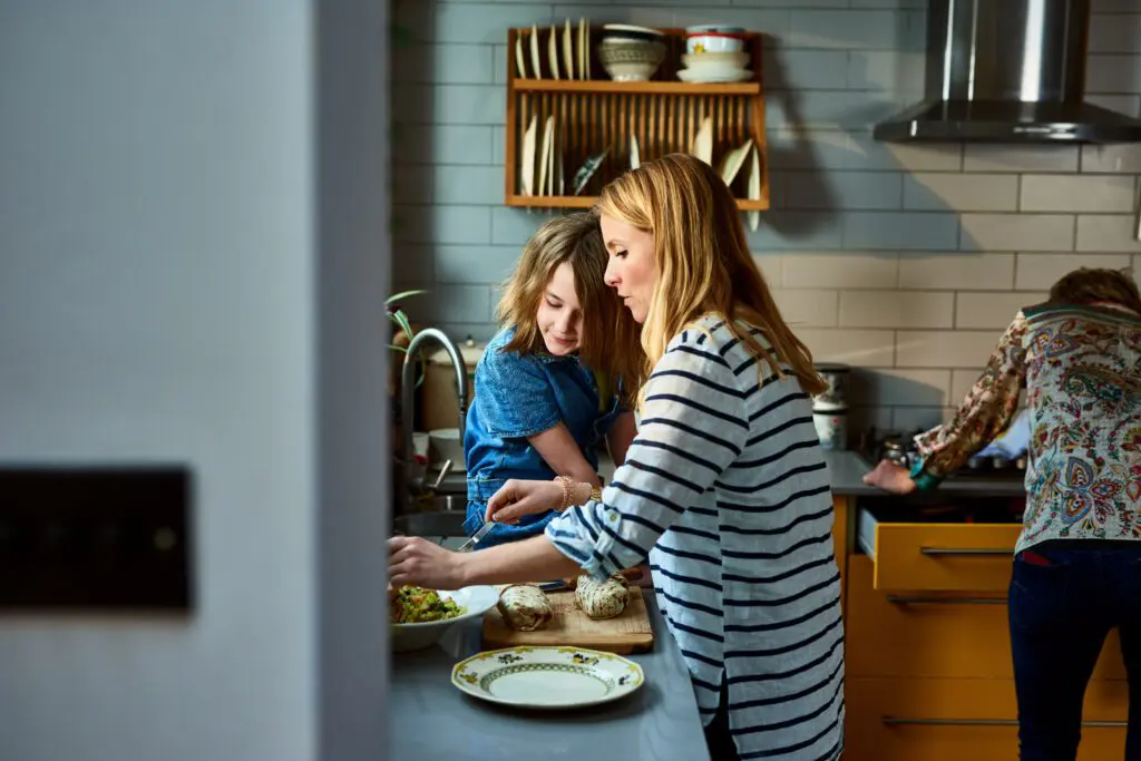 Side view of mother preparing food, daughter sitting on kitchen counter.